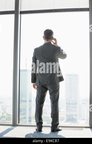 Voller Länge Rückansicht des Reifen Geschäftsmann mit Handy-weiß stehen in der Nähe von Fenster Stockfoto