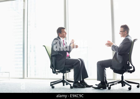 Full-length Seitenansicht der Unternehmer diskutieren beim Sitzen auf Bürostühlen durch Fenster Stockfoto