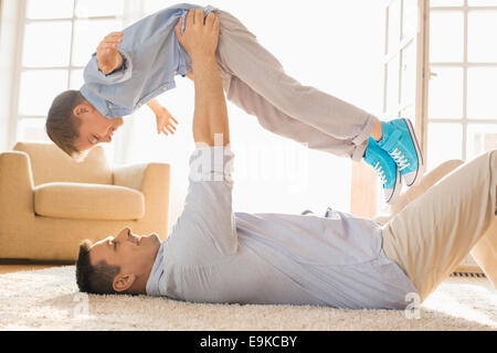 Seitenansicht des spielerischen Vater Sohn liegend am Boden zu Hause heben Stockfoto