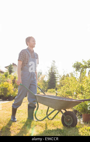 Der Mann schob Schubkarre im Garten in voller Länge Stockfoto