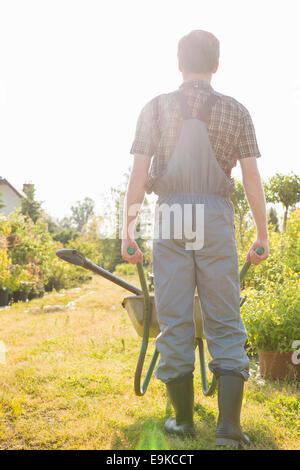 Full-length Rückansicht des Gärtners drücken Schubkarre im Garten Stockfoto