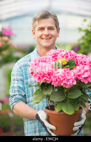 Porträt von glücklicher Mann hält Blumentopf im Gewächshaus Stockfoto