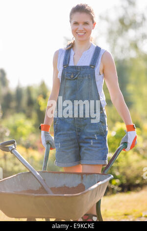 Porträt von glücklich weibliche Gärtner drücken Schubkarre im Garten Stockfoto