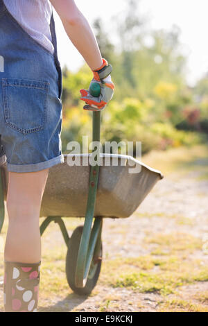 Mittelteil Rückansicht des weiblichen Gärtner pushing Schubkarre in Gärtnerei Stockfoto