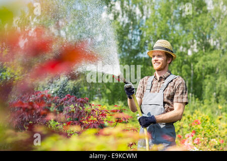 Lächelnd Mann Bewässerung von Pflanzen im Garten Stockfoto