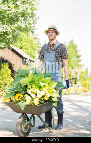 In voller Länge des Gärtners drücken Schubkarre mit Pflanzen im Garten Stockfoto