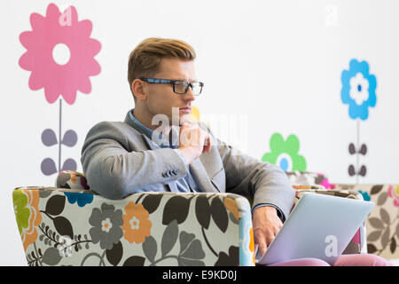 Mittleren Erwachsenenalter Geschäftsmann mit Laptop auf Sessel in Kreativbüro Stockfoto