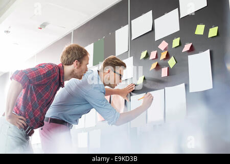 Geschäftsleute, die Analyse von Dokumenten an Wand im Büro Stockfoto