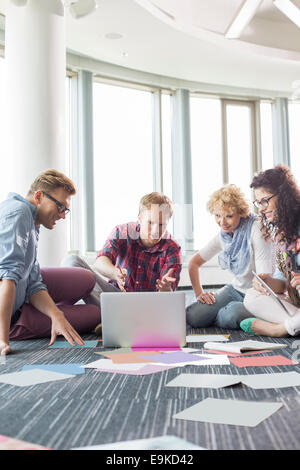 Geschäftsleute, die mit Laptop sitzend auf Etage an Kreativbüro Stockfoto