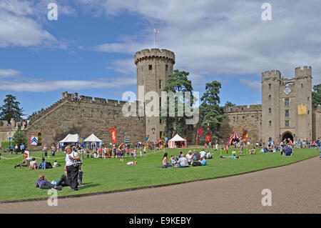 Viele Leute sitzen in der Sonne auf dem Rasen außerhalb Warwick Castle, England, UK. Stockfoto