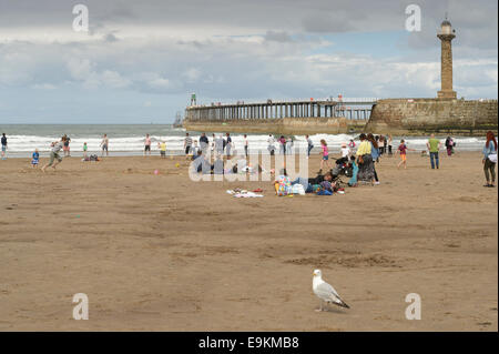 Urlauber am Strand auf einer bedeckt einen bewölkten Sommertag in der Nähe von Whitby Pier, N Yorks, UK. Stockfoto