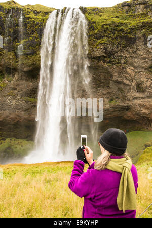 Frau, die ein Bild der Wasserfall Seljalandsfoss mit Handy. Süd-Island Stockfoto