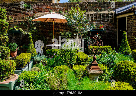 Ein weißes Gusseisen Stuhl- und geschützt durch einen Sonnenschirm bieten einen bequemen Platz, um die Blüten in einem elisabethanischen Garten anzeigen Stockfoto