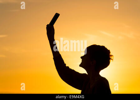 Eine Silhouette Mädchen hält ein Handy in die Luft zu versuchen und ein Datensignal erhalten. Stockfoto