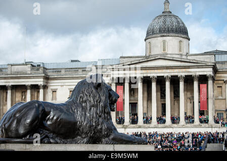 LONDON, Vereinigtes Königreich – eine der vier großen bronzenen Löwenstatuen, bekannt als die Landseer Lions, am Fuße der Nelson's Column am Trafalgar Square im Zentrum von London. Im Hintergrund steht die Nationalgalerie, die eine der weltweit besten Sammlungen westeuropäischer Gemälde beherbergt. Stockfoto