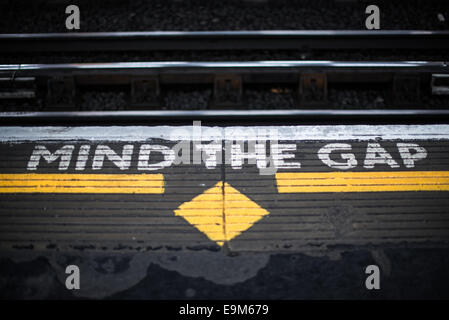 LONDON, Vereinigtes Königreich – lackierte Schilder auf einem Bahnsteig der Londoner U-Bahn warnen die Passagiere, beim ein- und Aussteigen den Zug zwischen dem Zug und dem Bahnsteig zu „Mind the Gap“ zu verlassen. Dieser legendäre Satz ist im gesamten Londoner U-Bahn-System zu sehen und gewährleistet die Sicherheit der öffentlichen Verkehrsmittel in der ganzen Stadt. Stockfoto