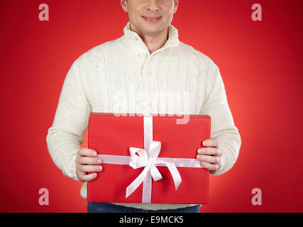 Lächelnd Mann in weißer Pullover mit roten Geschenkbox mit Seidenband gebunden Stockfoto