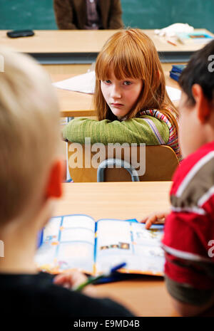 Eine Mädchen dreht sich zurück und starrt auf zwei Jungs in einem Klassenzimmer Stockfoto