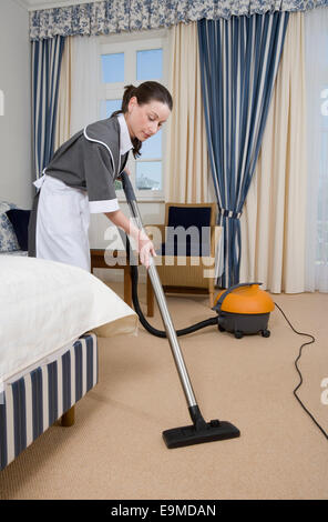 Uniformierte Dienstmädchen mit Staubsauger im Hotelzimmer Stockfoto