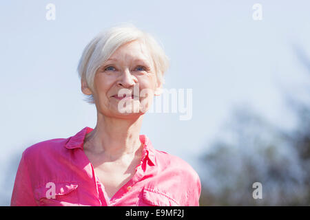 Reife Frau lächelnd während wegschauen gegen Himmel Stockfoto