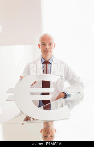 Porträt von zuversichtlich Arzt hält Euro-Symbol am Schalter in Klinik Stockfoto