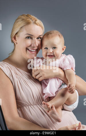 Porträt der glückliche Mutter mit niedlichen Babymädchen vor grauem Hintergrund Stockfoto