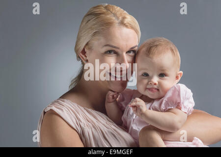 Porträt der glückliche Mutter mit niedlichen Babymädchen vor grauem Hintergrund Stockfoto