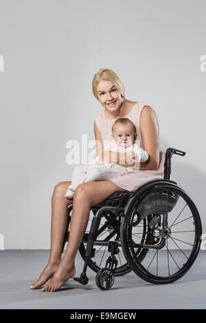 In voller Länge Portrait von glücklich Frau mit Tochter im Rollstuhl vor grauem Hintergrund Stockfoto