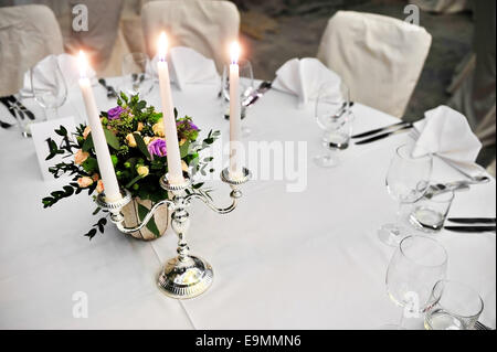Leuchter mit brennenden Kerzen und Blumenschmuck auf eleganten Esstisch Stockfoto