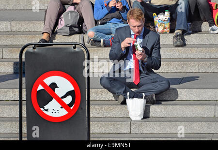 London, England, Vereinigtes Königreich. Mann isst auf den Stufen der National Gallery am Trafalgar Square. 'Nicht die Tauben füttern' Zeichen Stockfoto