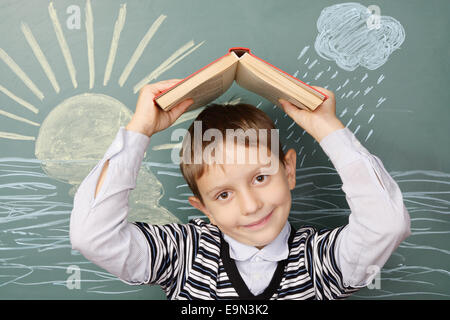 Ungewöhnliche Bildungskonzept. Junge unter Dach aus Buch auf Grund der Kreidezeichnung von Sonne und Regen. Stockfoto