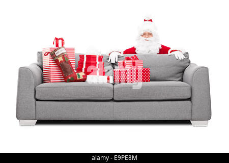 Santa Claus versteckt sich hinter einem Sofa voller Weihnachtsgeschenke isoliert auf weißem Hintergrund Stockfoto