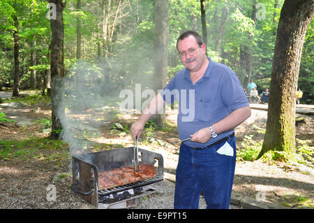 Ein Mann mittleren Alters kocht Hamburger und Hotdogs mit vielen Barbecue Sauce auf einem Holzkohlegrill im Great-Smoky-Mountains-Nation Stockfoto