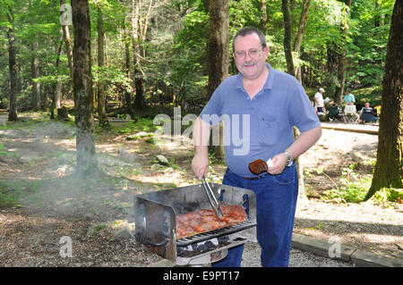 Ein Mann mittleren Alters kocht Hamburger und Hotdogs mit vielen Barbecue Sauce auf einem Holzkohlegrill im Great-Smoky-Mountains-Nation Stockfoto