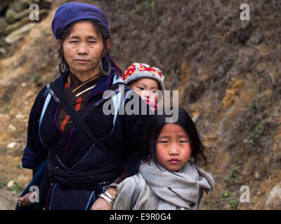 Hmong Frau in traditioneller Kleidung, mit Baby und kleinen Tochter auf dem Weg zur Ta Van Dorf in der Nähe von Sapa, Lao Cai, Vietnam. Stockfoto