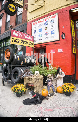 New York, USA. 31. Oktober 2014.  mechanisierte Halloween Ghule Kürbisse & Töpfe der gelben Chrysanthemen begleiten Sie Rack von Neureifen Reifen auf Bürgersteig vor lokalen Autowerkstatt am Morgen von All Hallows Eve Credit: Dorothy Alexander/Alamy Live News Stockfoto