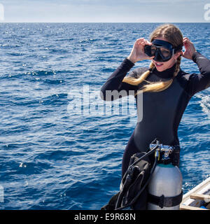 Kaukasische Frau in Neoprenanzug auf einem Boot setzen auf Schutzbrillen in Vorbereitung zum Tauchen. Stockfoto