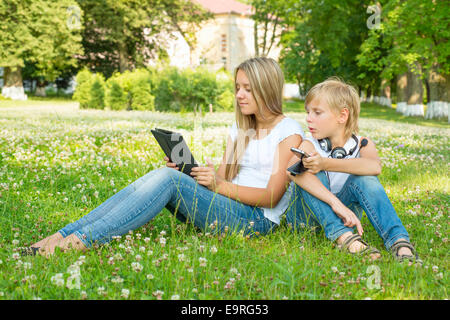 Jungen und Mädchen im Park sitzen und genießen Sie die Tablette Stockfoto