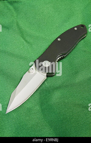 Klappmesser mit einem schwarzen Griff und Schloss auf grünen Leinwand Stockfoto