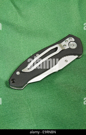 Klappmesser mit einem schwarzen Griff und Schloss auf grünen Leinwand Stockfoto