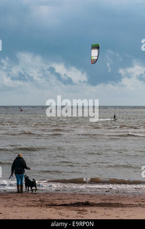 Ein Kitesurfer an einem windigen Tag in Exmouth in Devon, England. Gute Bedingungen zum Kitesurfen. Eine Frau und ihr Hund zu sehen, vom Strand entfernt Stockfoto