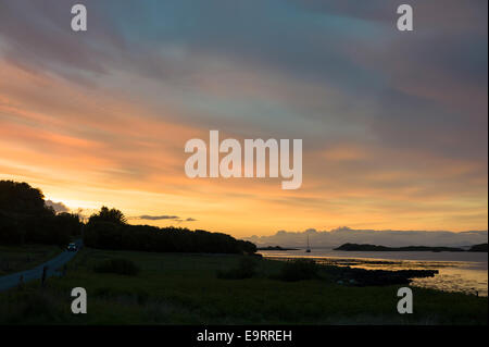 Skyscene der untergehende Sonne über einsame Fischerboot auf Dunvegan Loch und Auto vorbei auf Feldweg, der Isle Of Skye in Scotlan Stockfoto