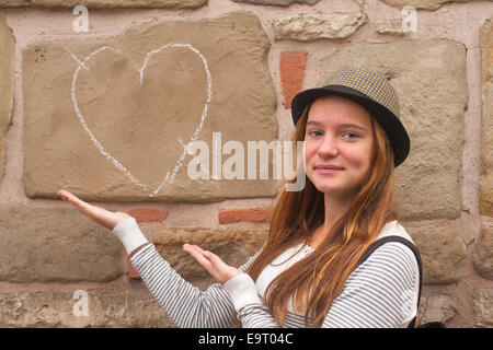 Süße junge Mädchen in der Nähe einer Wand gemalt Kreide Herz und Pfeil. Fallen in Liebe Konzept. Stockfoto