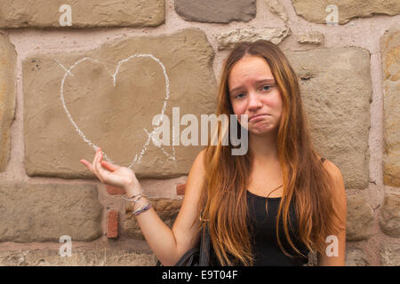 Traurige junge hübsche Mädchen und Herz mit Kreide an die Wand. Gebrochene Liebe Konzept. Stockfoto