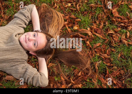Сute Mädchen auf Laub im Herbst Park liegen. Stockfoto
