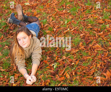 Junge süße Mädchen auf gelbes Laub im Herbst Park liegen. Stockfoto