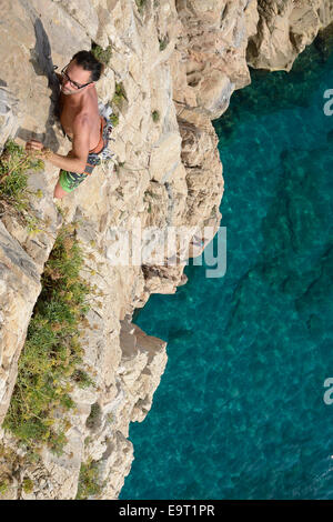 Junger Kletterer auf einer Klippe hoch über dem azurblauen Mittelmeer. Capo Noli, Provinz Savona, Ligurien, Italien. Stockfoto