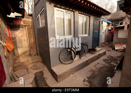 Ein Fahrrad ruht neben einem renovierten Hutong-Haus mit festlichen roten Türdekorationen. Peking, China Stockfoto