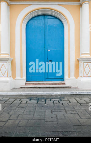 Große gewölbte hellblaue Holztüren mit einer kleineren Tür, die in die rechte Tür geschnitten ist, setzen sich zwischen dekorativen Säulen auf gelbem Stuckhaus. Stockfoto