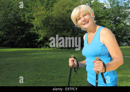 Eine ältere Frau Nordic Walking mit Kopfhörer Stockfoto